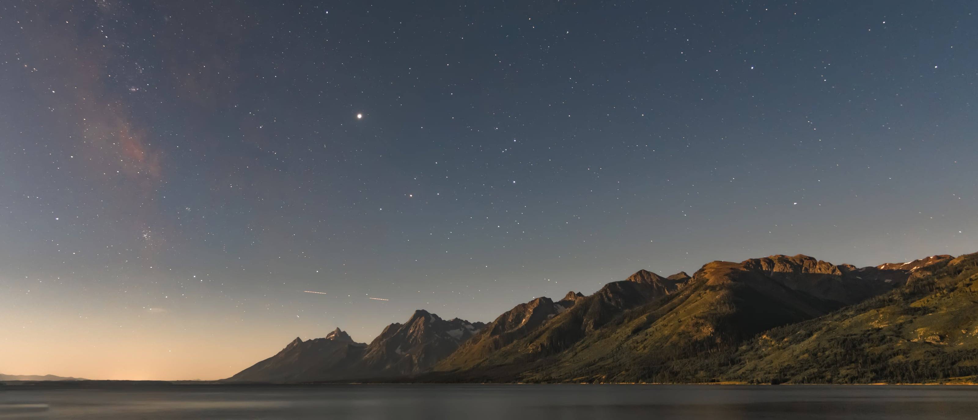Dawn breaking over the Teton Range, the first warm light low on the horizon under a fading field of stars.