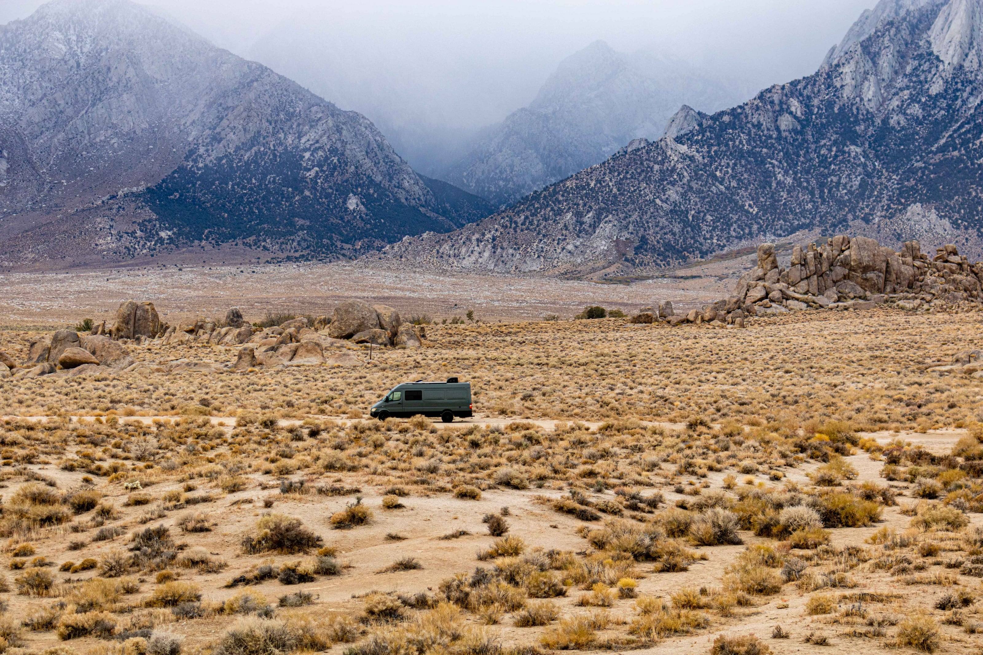 A green Sprinter van crossing the high desert of the Alabama Hills as a storm settles on the Sierra Nevada behind it.
