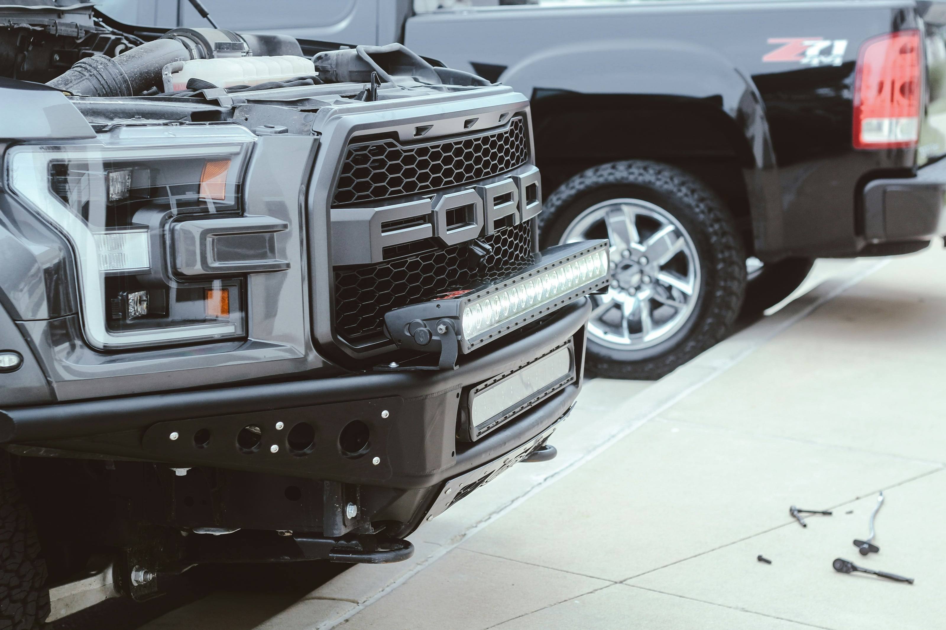 A steel front bumper and light bar being fitted to a pickup in a shop, tools still on the floor.