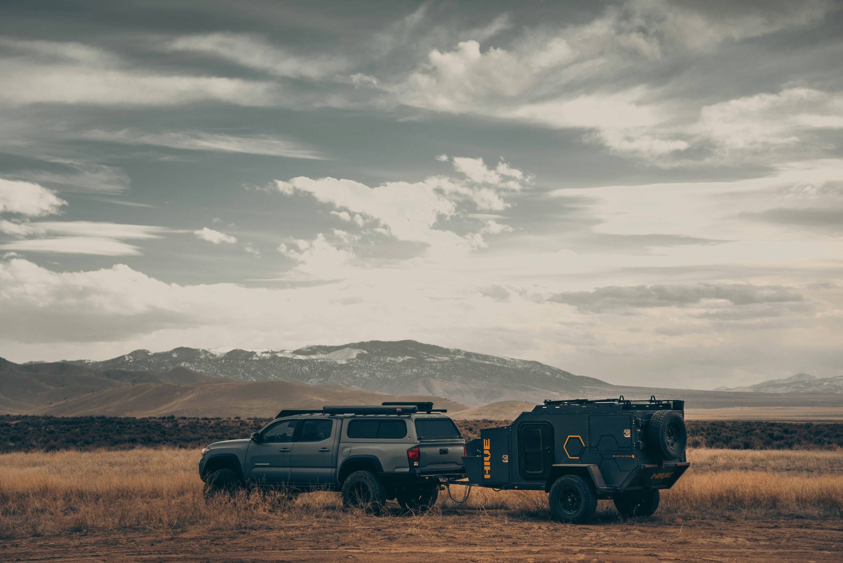 A Toyota Tacoma towing an off-road trailer across a sagebrush basin under a broken sky.