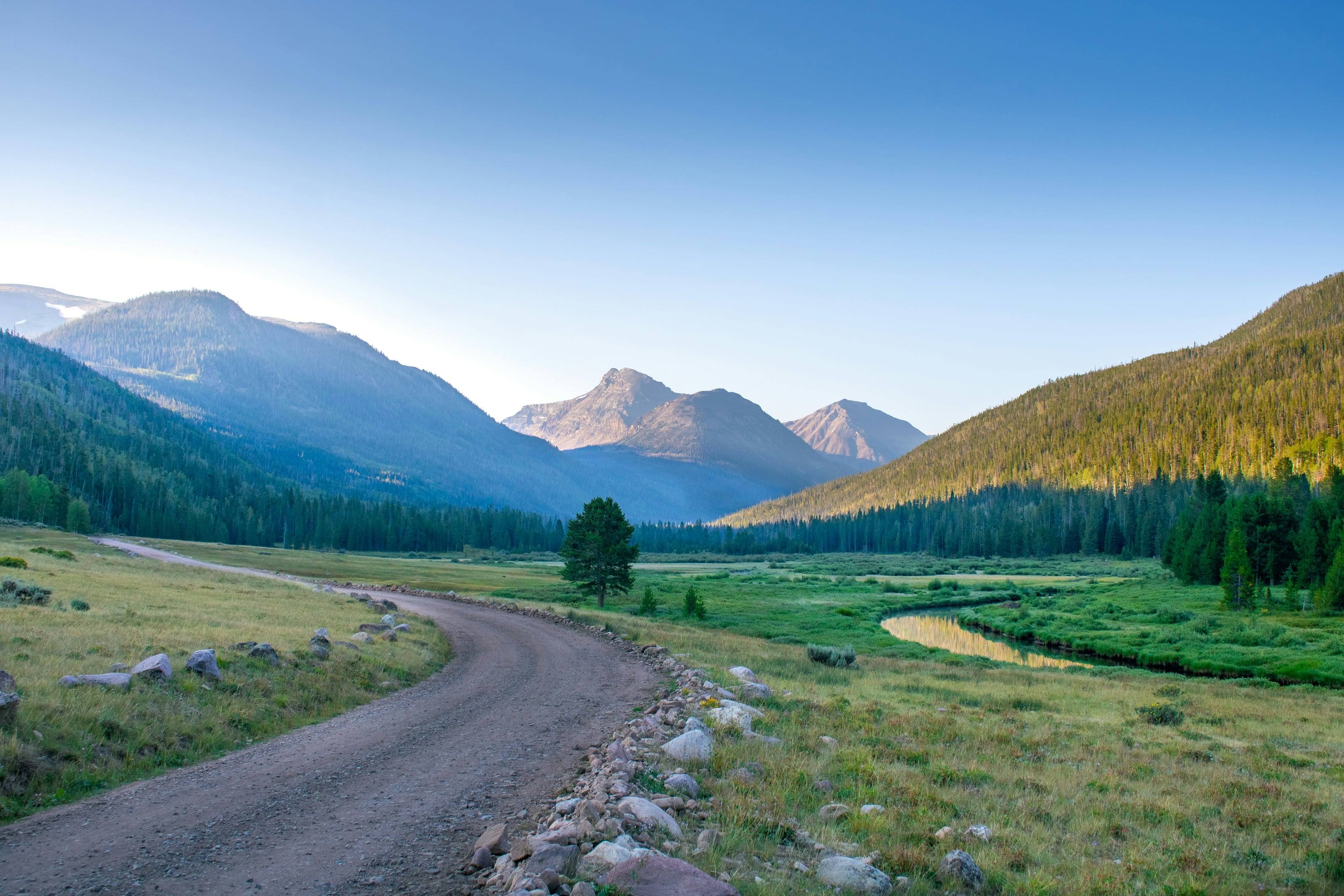 A gravel road curving into a high mountain valley at first light, the peaks catching the sun.