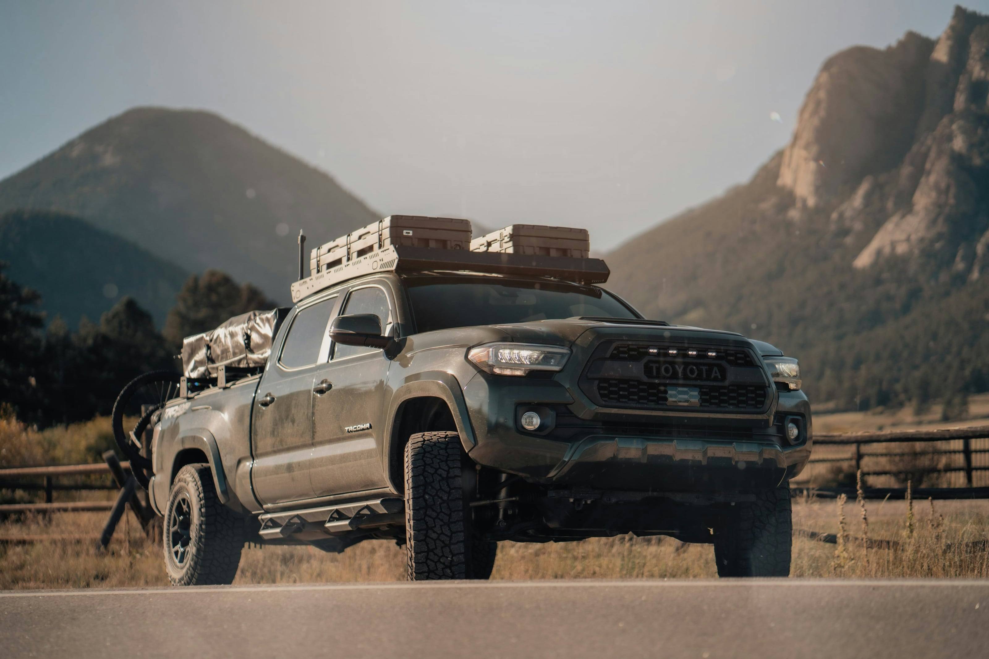 A Tacoma loaded with roof cases and gear at the edge of a mountain meadow.