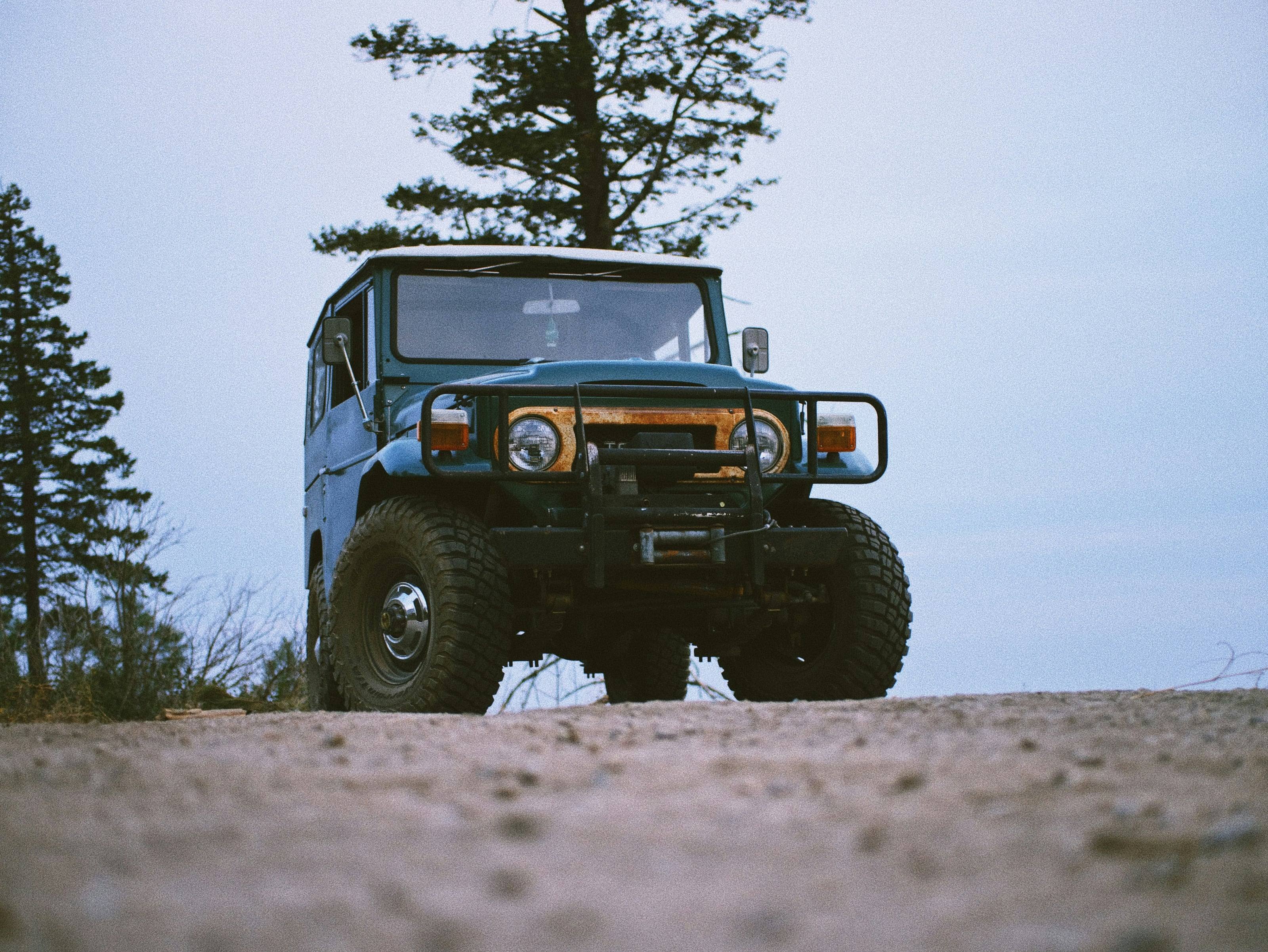 A classic FJ40 Land Cruiser with a winch bumper on a dirt track at dusk.