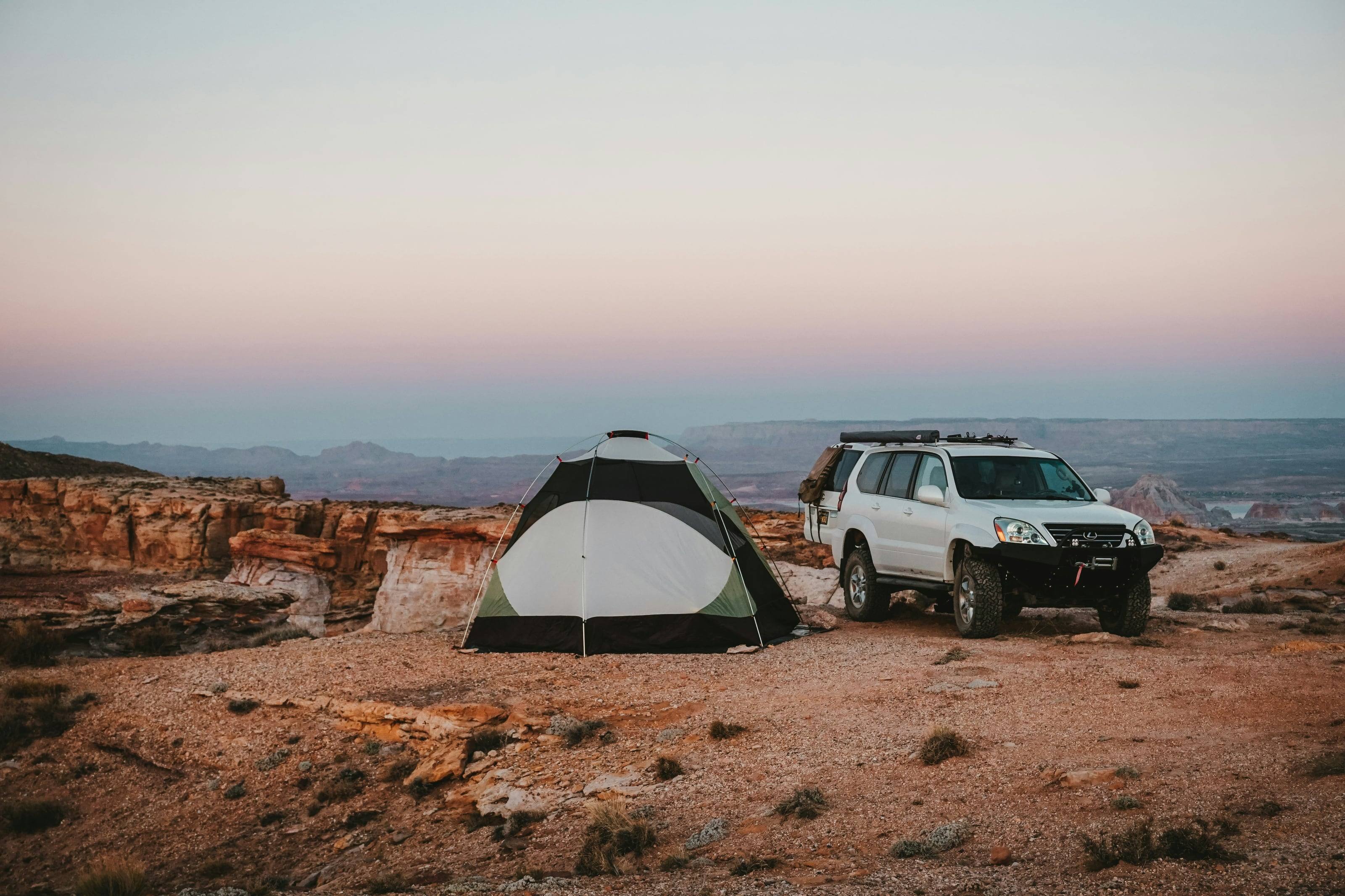 A Lexus GX parked beside a tent on a red rock overlook at dusk.