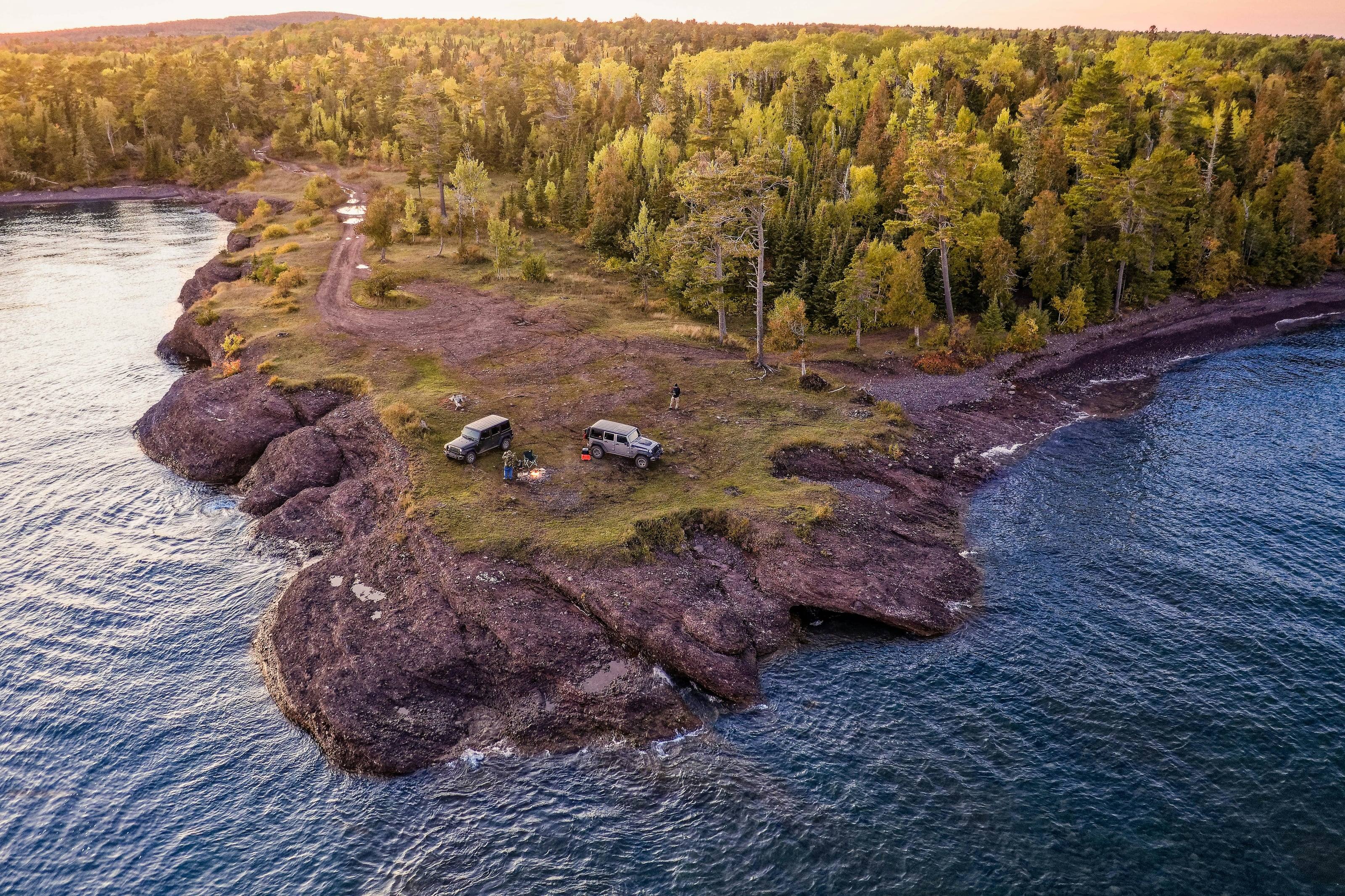 Two vehicles camped on a rocky point above a big lake, seen from the air, the first fall color in the trees.