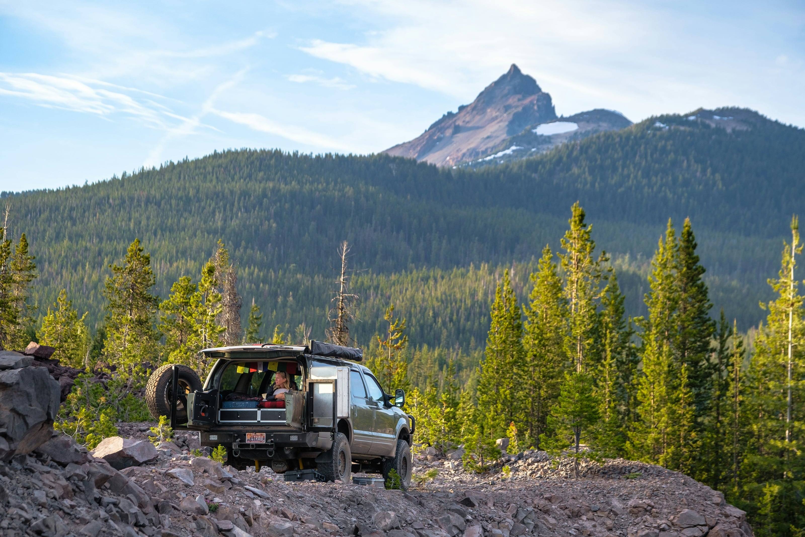 A 4x4 with a roof tent parked on a rocky forest track below a volcanic spire.